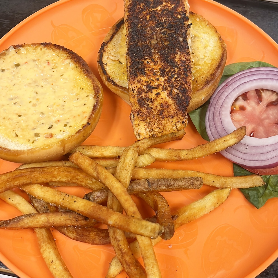 Lutfi’s Raymore seafood sandwich with a toasted bun, grilled fish, lettuce, tomato, onion, and fries.